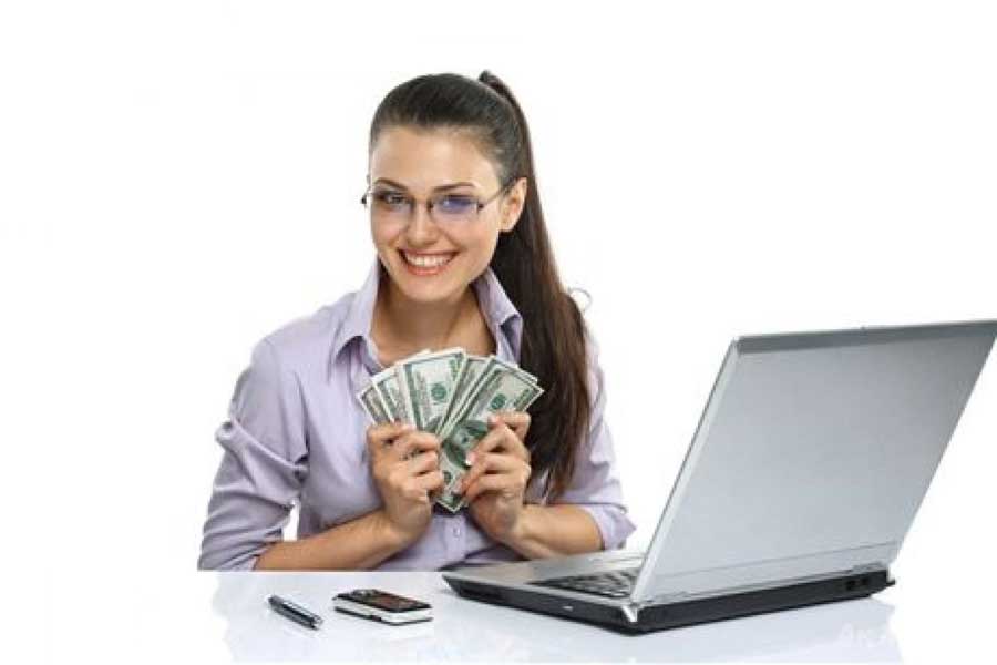 Девушка с деньгами в руках за столом у компьютера